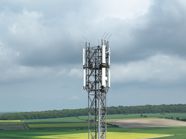 Mobilfunkmasten auf einem Feld mit Bergen im Hintergrund.