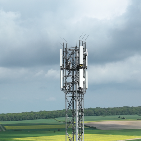 Mobilfunkmast in ländlicher Umgebung, umgeben von Wiesen und Hügeln.